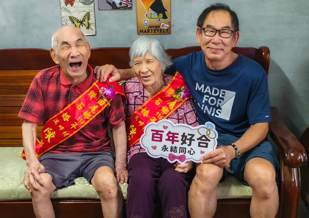 老夫妻戴著表揚彩帶笑得開懷,家人拿著「百年好合 永結同心」牌子