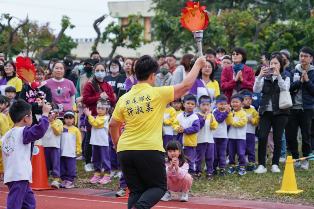 鄉長穿黃色上衣,高舉火炬,旁邊孩子與家長圍觀