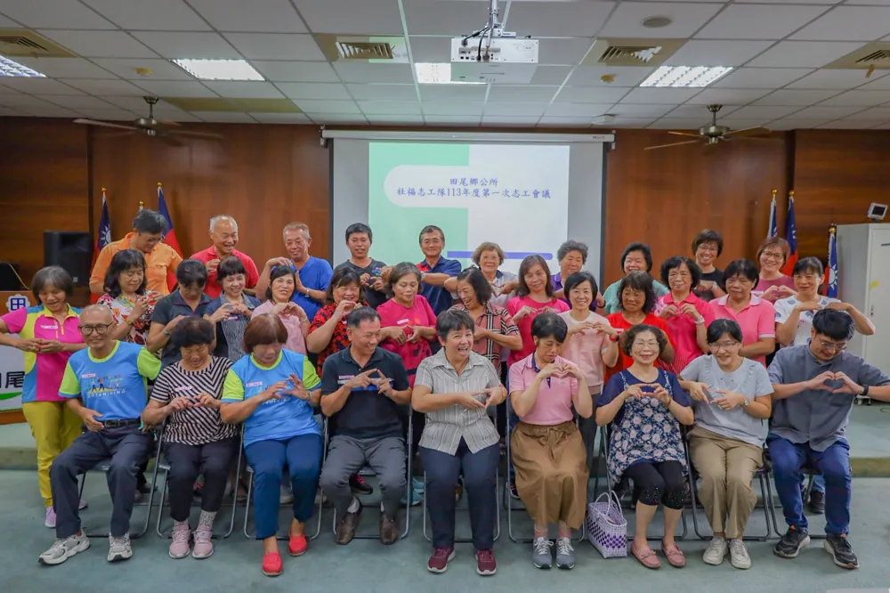 志工們坐在會議室裡,一起比出愛心手勢