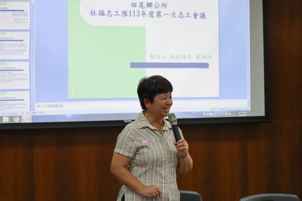 鄉長站在投影幕前,拿麥克風對志工說明