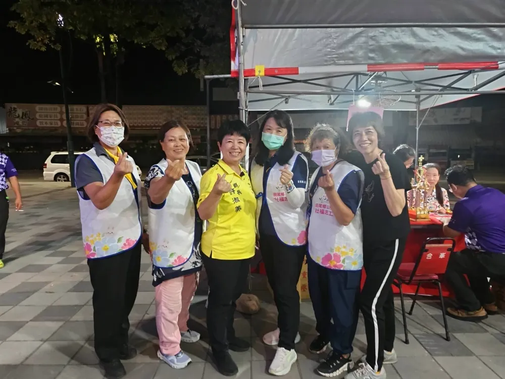 夜晚的廣場上,鄉長與穿著「社福志工」背心的志工們比出愛心